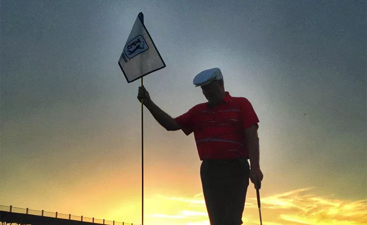 Tom Weiskopf on golf green holding pin at sunset