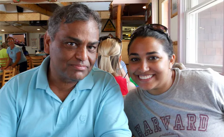 Paula Mukherjee (right) with her dad Sanjib (right), sitting in a booth at a restaurant smiling.