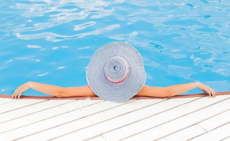 Feature image Woman lounging in swimming pool wearing a hat to protect her face and scalp from sun exposure
