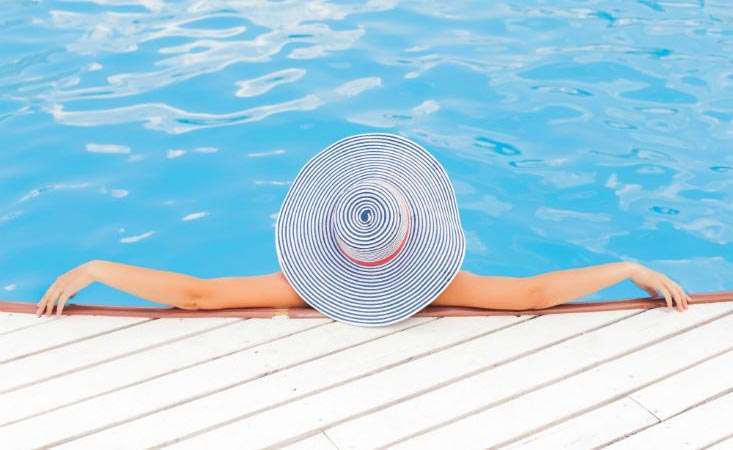 Woman lounging in swimming pool wearing a hat to protect her face and scalp from sun exposure