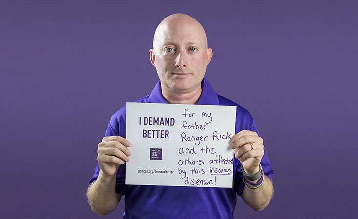 Volunteer and advocate holds a sign saying why he Demands Better for pancreatic cancer patients