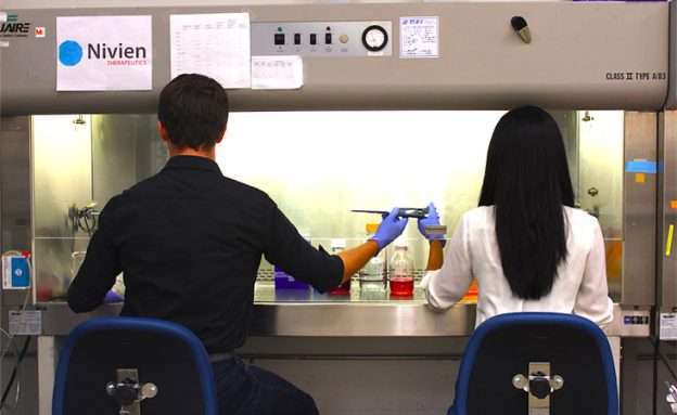 Feature image Co-founders of Nivien Therapeutics share a pipette in lab to test a new pancreatic cancer drug