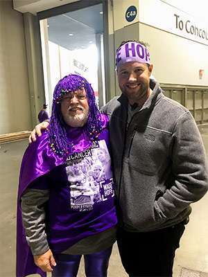 Man wearing purple wig volunteers at PurpleStride walks nationwide to end pancreatic cancer
