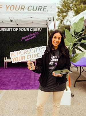 Sylvester Comprehensive Cancer Center staff member holds sign saying, 'In pursuit of your cure.TM (superscript TM) showing her support for pancreatic cancer patients.