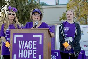Caucasian woman on podium addressing group of fundraisers at outdoor event.