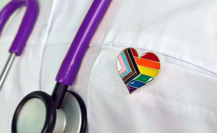 Feature image close up of doctor wearing LGBTQ+ pride pin and stethoscope