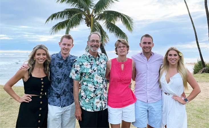 Feature image A family of six people – three women, three men – posing for the camera on a tropical beach.