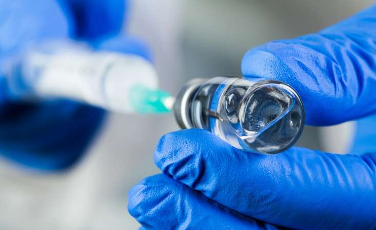 Feature image closeup of hands wearing blue rubber gloves holding a vial and syringe