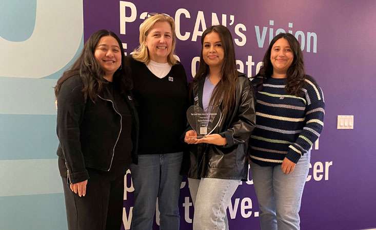 Feature image PanCAN staff member Abigail Dominguez, Lisa Kulok, 2024 awardee Karina Gutierrez, and last year’s awardee Brianne Flores all standing together posing for the picture in front of a purple wall with writing on it.