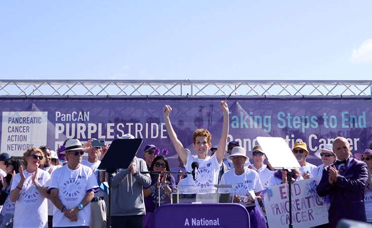 Feature image Twenty-year pancreatic cancer survivor Kitty Swink on stage at PurpleStride Los Angeles 2024 with dozens of survivors.