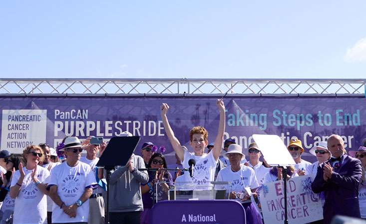 Twenty-year pancreatic cancer survivor Kitty Swink on stage at PurpleStride Los Angeles 2024 with dozens of survivors.