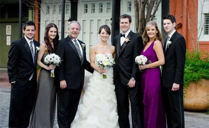 Feature image Family of four men and three women, including the bride in her dress, pose for a wedding photo.