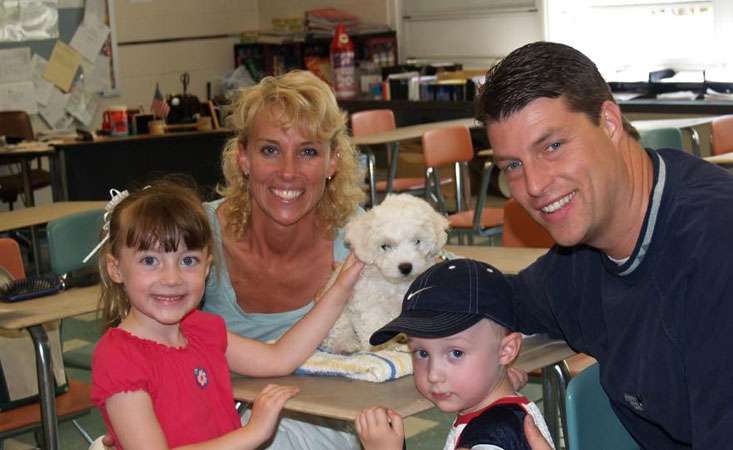 Feature image A mother, father, daughter and son inside a classroom smiling for the camera.